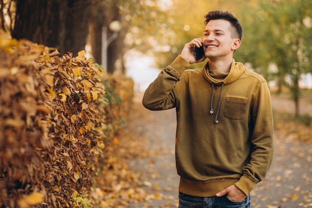 Retrato de chico guapo y feliz sonriendo y hablando por teléfono en el parque de otoño