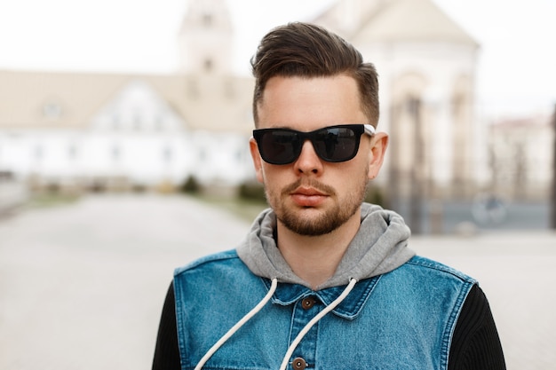 Retrato de un chico guapo con gafas de sol y una chaqueta vaquera en la ciudad