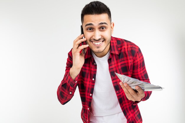 Retrato de un chico guapo con un montón de dinero hablando por teléfono en un estudio blanco con espacio de copia