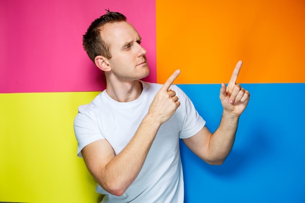 Retrato de un chico joven y alegre sobre un fondo multicolor, vestido con una camiseta blanca, crea un peinado de moda, emociones positivas