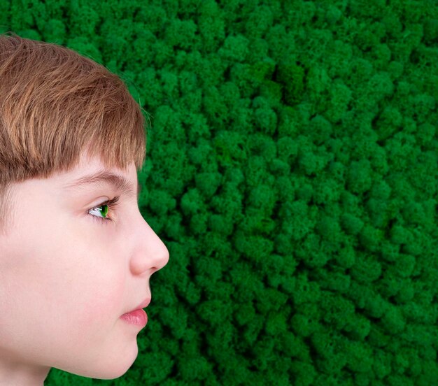 Retrato de un chico lindo con ojos verdes contra un fondo de pared de plantas verdes