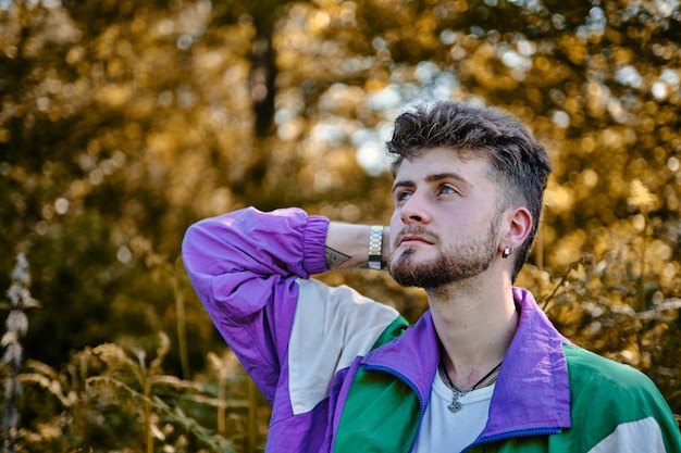 Retrato de un chico de moda con piercings pensativo mirando al cielo con la mano en el cuello