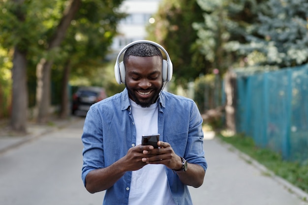 Retrato de chico sonriente en auriculares y teléfono móvil al aire libre