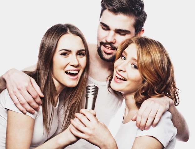 Retrato de chicos y chicas felices cantando en el micrófono sobre fondo blanco.