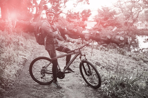 Retrato de ciclista de montaña masculino con bicicleta en el bosque