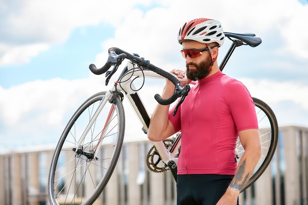 Retrato de un ciclista parado debajo de un puente con una bicicleta en la mano posando a la cámara contra un fondo de arquitectura Estilo de vida activo El ciclismo es un pasatiempo