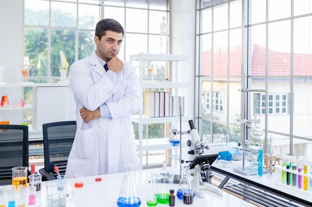 Retrato científico confiado de un científico feliz que mantiene los brazos cruzados en un científico de laboratorio químico que sostiene un tubo de ensayo con una muestra en el fondo del análisis de laboratorio