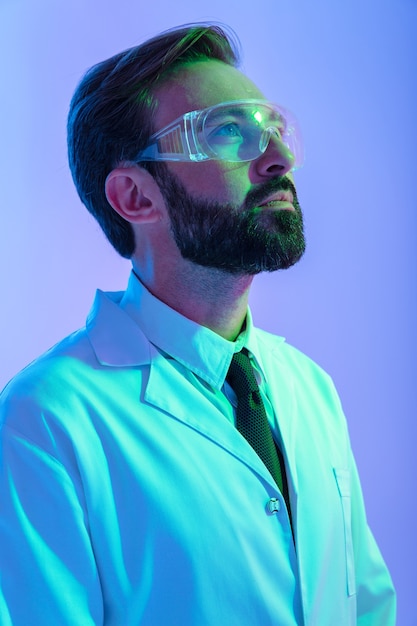 Retrato de un científico joven confiado en uniforme y gafas que se encuentran aisladas sobre neblina rosa-azul, mirando a otro lado