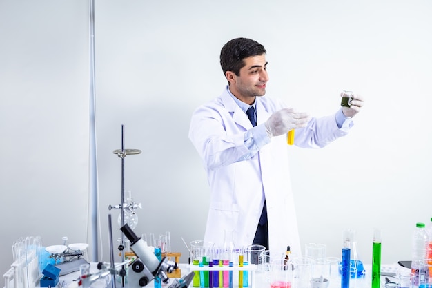 Retrato de científico seguro de científico masculino feliz en un científico de laboratorio de química con tubo de ensayo con muestra en el fondo de análisis de laboratorio