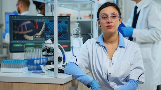 Retrato de científico sonriendo a la cámara sentado en un moderno laboratorio equipado. Equipo multiétnico que examina la evolución del virus utilizando herramientas de alta tecnología y química para la investigación científica, desarrollo de vacunas