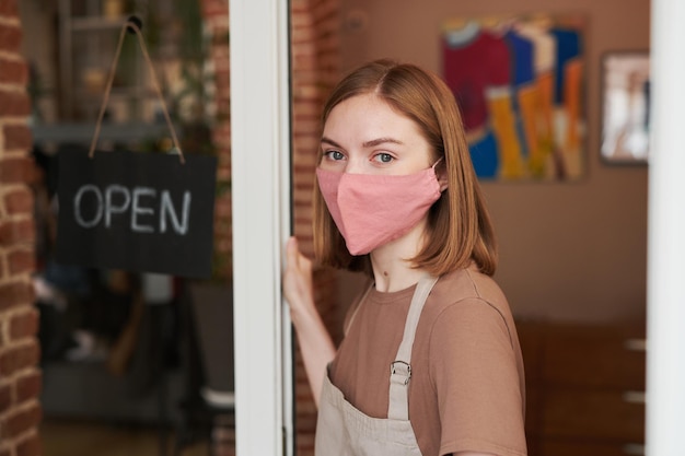 Retrato de cierre medio horizontal de una joven caucásica con máscara protectora en la cara que comienza la jornada laboral con café de apertura