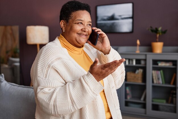 Retrato en la cintura de una alegre abuela mayor hablando por teléfono en casa y gesticulando