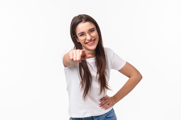 Retrato de cintura para arriba de entusiasta, feliz divertida joven de 20 años en camiseta y gafas, riendo a carcajadas divirtiéndose, señalando con el dedo a la cámara como bromeando