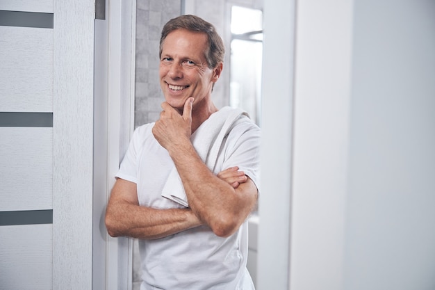 Retrato de cintura para arriba de un hombre feliz en una camiseta apoyando su barbilla en su mano