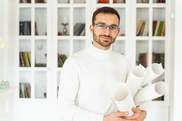 Retrato de cintura para arriba de un ingeniero masculino complacido sosteniendo rollos de papel de dibujo en sus manos