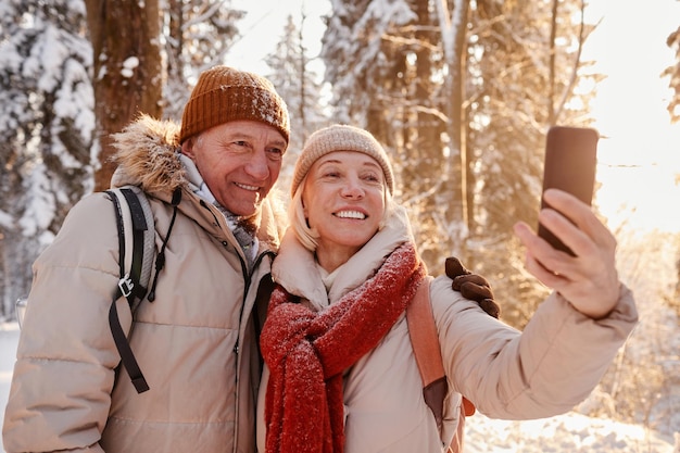 Retrato de cintura arriba de una pareja feliz tomando una foto selfie mientras disfruta de una caminata en el bosque invernal co