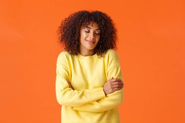 Retrato en la cintura romántica encantadora joven soñando con viajar a un lugar cálido en vacaciones de invierno, cerrar los ojos y sonreír sensualmente, abrazando su propio cuerpo, de pie naranja