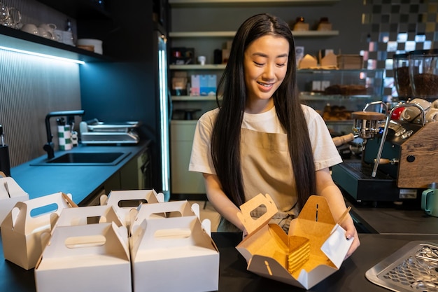 Retrato de cintura de un trabajador satisfecho empaquetando una rebanada de pastel de crema en la caja de cartón en el mostrador