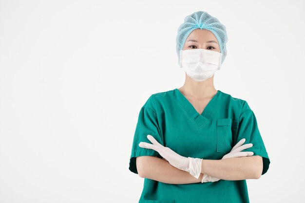 Retrato de una cirujana con guantes de exfoliación, sombrero y máscara médica cruzando los brazos y mirando a la cámara