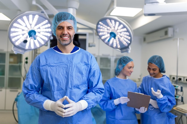 Foto retrato de un cirujano masculino de pie con los brazos cruzados en el quirófano del hospital los cirujanos del equipo están realizando una operación el médico de mediana edad está mirando la cámara en un quirófano moderno