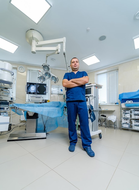 Retrato del cirujano profesional mirando a la cámara y sonriendo después de una operación exitosa. En el fondo moderno quirófano del hospital.