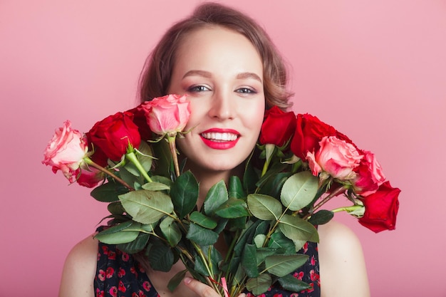 Retrato de clausura de una linda y atractiva dama morena escondida detrás de flores de colores sobre fondo rosa