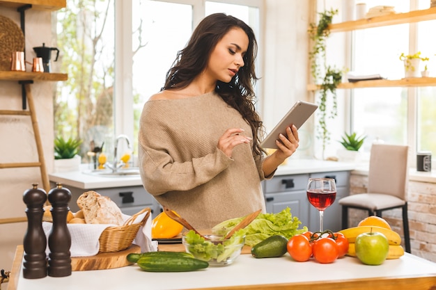Retrato de cocinar comida sana mujer joven en la cocina buscando una receta en Internet. Usando tableta.