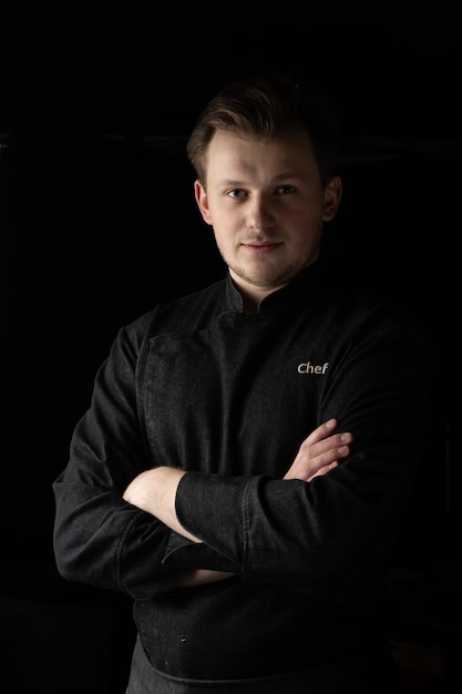 Retrato de un cocinero cocinero en una chaqueta sobre un fondo oscuro
