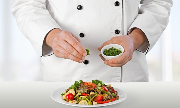 Retrato de un cocinero cocinero masculino preparando ensalada aislado sobre un fondo blanco.