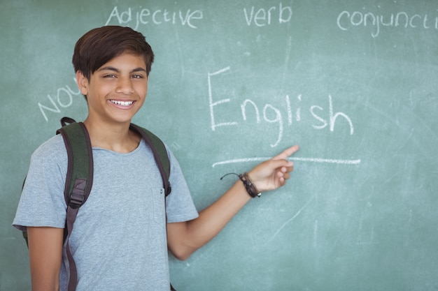 Retrato de colegial feliz apuntando a la pizarra en el aula