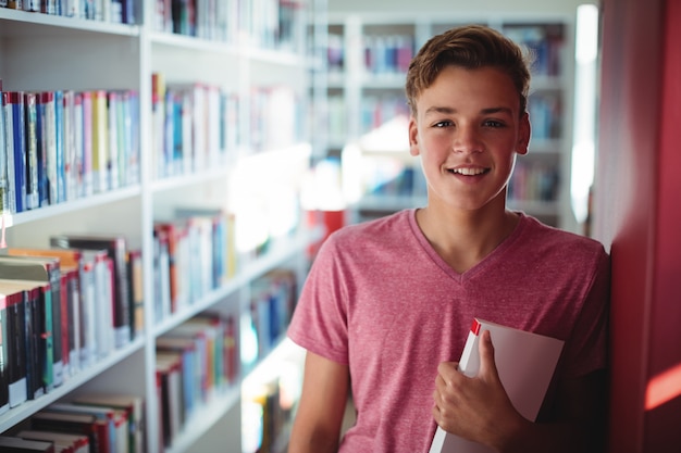Retrato de colegial feliz sosteniendo el libro en la biblioteca