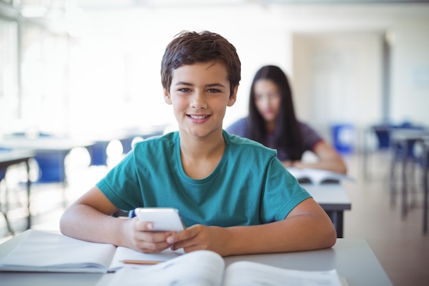 Retrato de colegial mediante teléfono móvil mientras estudia en el aula