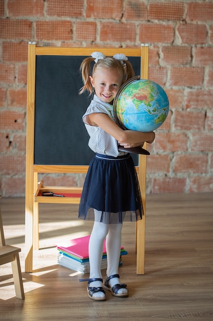 Retrato de colegiala caucásica de pie delante de la pizarra con globo en sus manos, concepto de regreso a la escuela