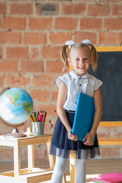 Retrato de colegiala caucásica de pie delante de la pizarra con el libro en sus manos, concepto de regreso a la escuela