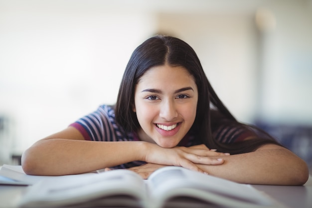 Retrato de colegiala feliz apoyado en un banco en el aula