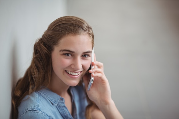 Retrato de colegiala feliz hablando por teléfono móvil en el pasillo