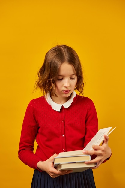 Retrato de una colegiala feliz leyendo un libro en un estudio amarillo