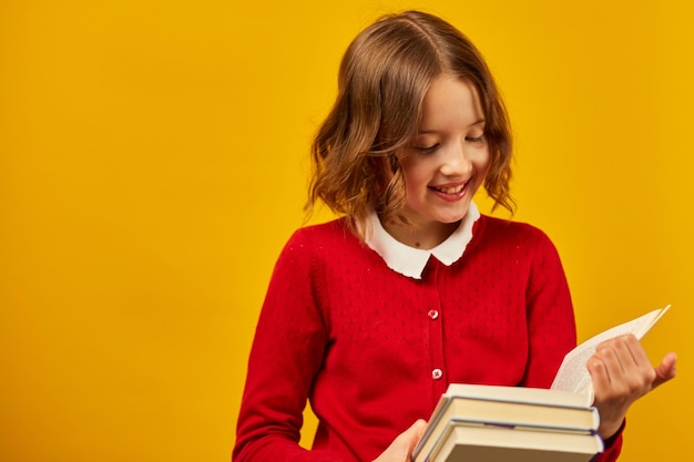 Retrato de una colegiala feliz leyendo un libro en un estudio amarillo