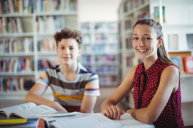 Retrato de colegiala feliz sentada con su compañera de clase en la biblioteca