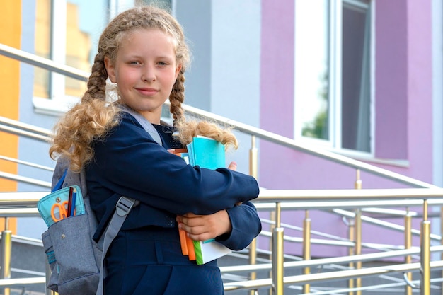 Retrato de una colegiala en el fondo de la escuela Días de escuela de concepto Regreso a la escuela niña en uniforme con una mochila alumno aprendiz erudito Un estudiante sostiene libros y cuadernos