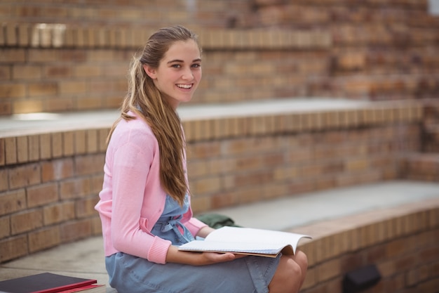 Retrato de colegiala leyendo un libro en el campus