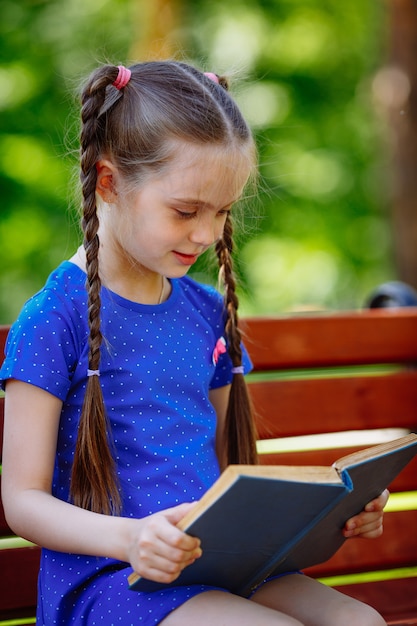 Retrato de colegiala en un libro de lectura de banco. Parque de la ciudad de fondo.