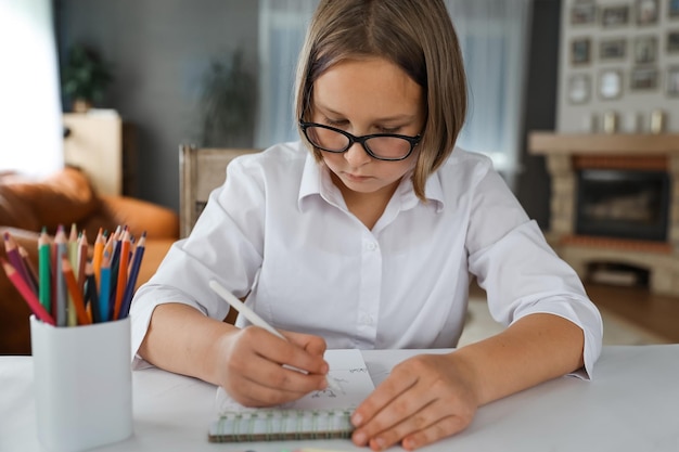 Retrato de la colegiala sentada en la mesa en el interior y haciendo su tarea La niña hace la tarea en casa Aprendizaje a distancia Lecciones de educación para la tarea