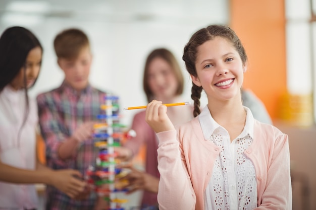 Retrato de colegiala sonriente sosteniendo un lápiz en el aula