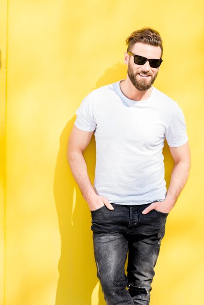 Retrato colorido de um homem bonito vestido de camiseta branca e jeans no fundo amarelo