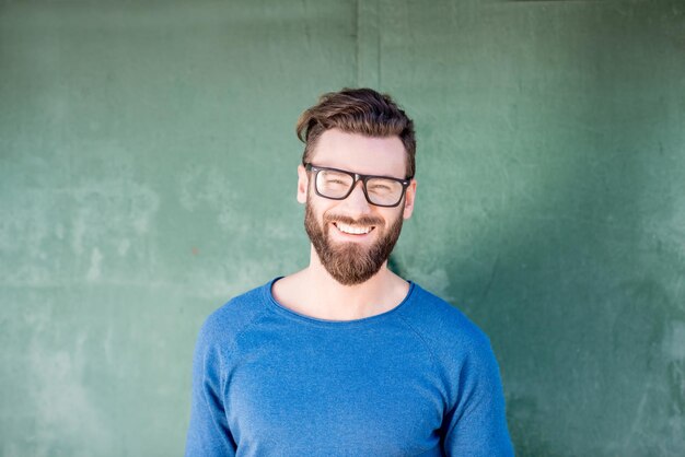 Retrato colorido de um homem bonito vestido de suéter azul em pé sobre o fundo verde da parede enferrujada