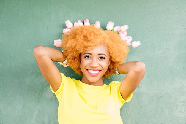 Retrato colorido de uma bela mulher africana segurando um buquê de tulipas no fundo da parede verde