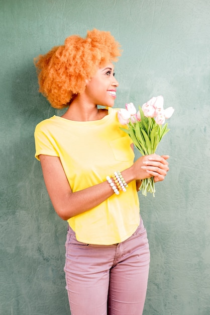 Retrato colorido de uma bela mulher africana segurando um buquê de tulipas no fundo da parede verde