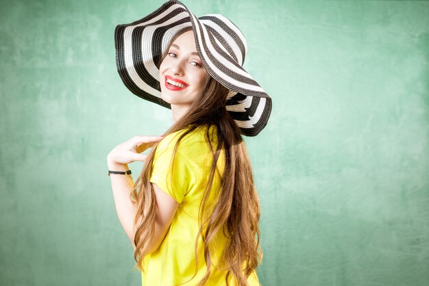 Retrato colorido de uma bela mulher em camiseta amarela e chapéu listrado sobre fundo verde