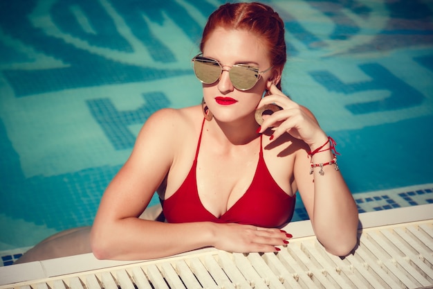 Retrato colorido de uma jovem bonita com maiô vermelho deitada perto da piscina